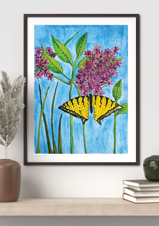A framed art print featuring a yellow and black swallowtail butterfly perched on pink-purple flowers with green leaves against a bright blue background, displayed on a shelf in a styled interior setting.