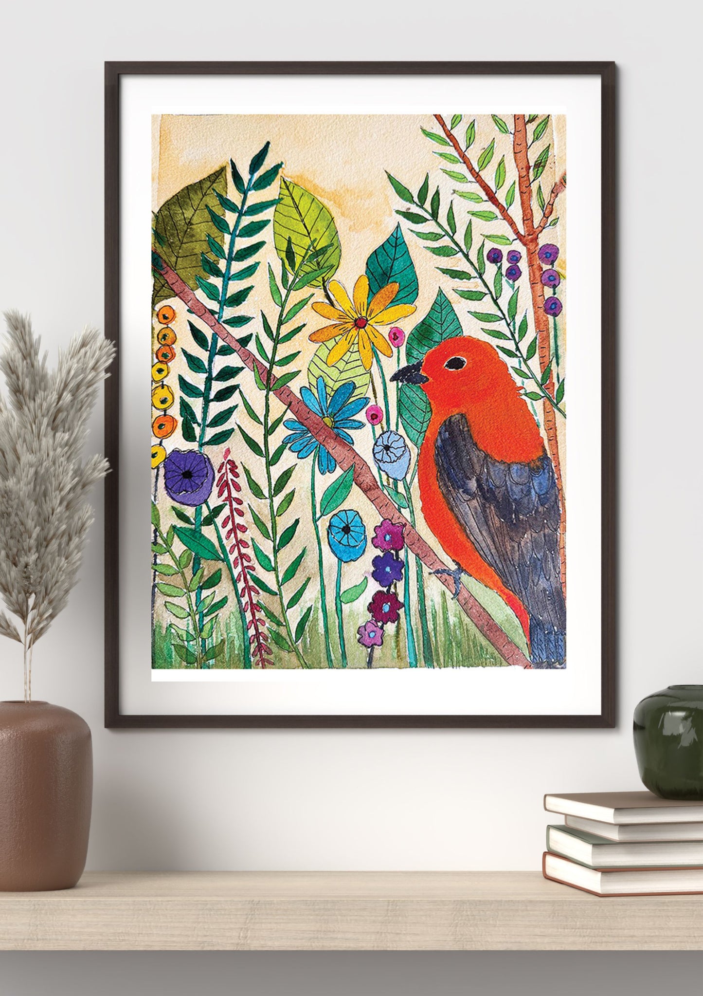 A framed botanical art print featuring a vibrant red bird among green leaves and colorful flowers, styled on a light wood shelf with a brown vase and books against a white wall.